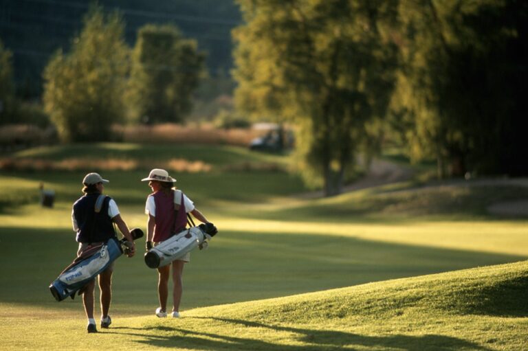 Two golfers walking to the next tee on a tree-lined golf course, highlighting the importance of a Tree Risk Management Strategy to ensure their safety from potential tree hazards